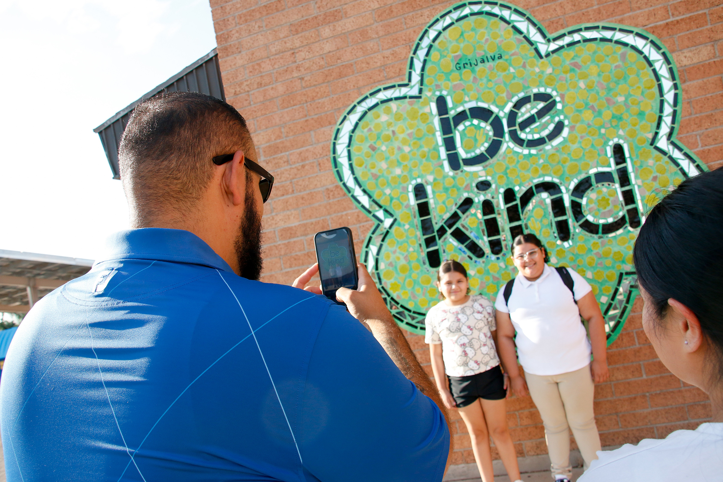 A dad takes a picture of his two daughters in front of the Be Kind mural