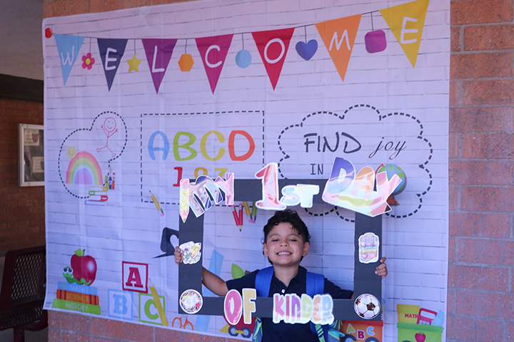 A boy holds up a frame reading my first day of kinder