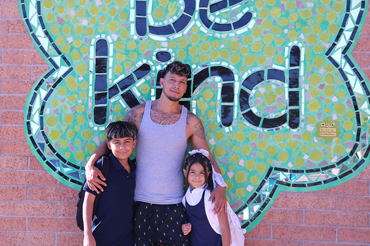 A dad and his son and daughter pose in front of the Be Kind mural