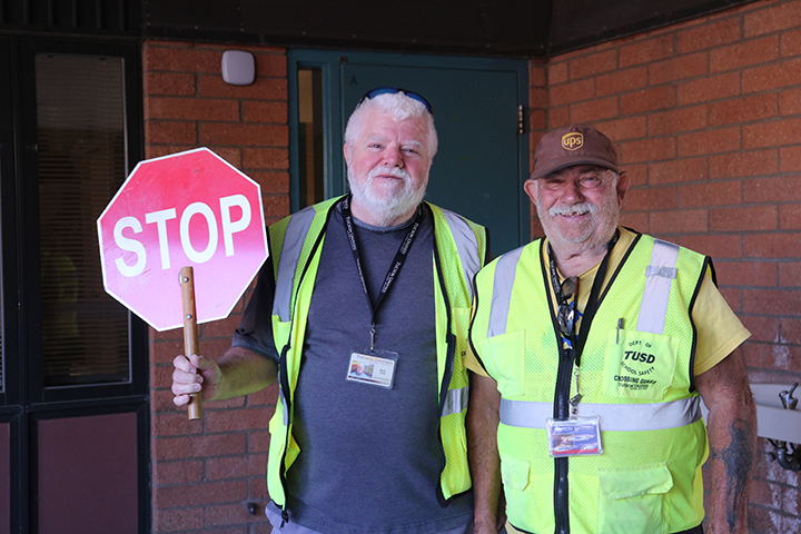 Two men in their yellow crossing guard vests smile for a photo