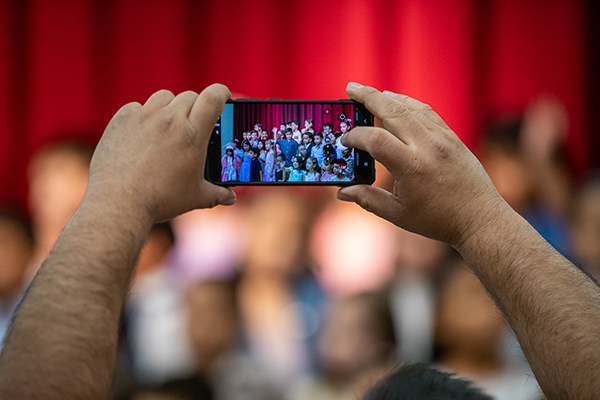 A man holds up his phone to take a video of the students performing