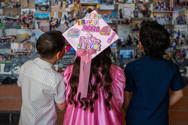 Two boys, left and right, and a girl, center wearing a pink graduation cap and gown